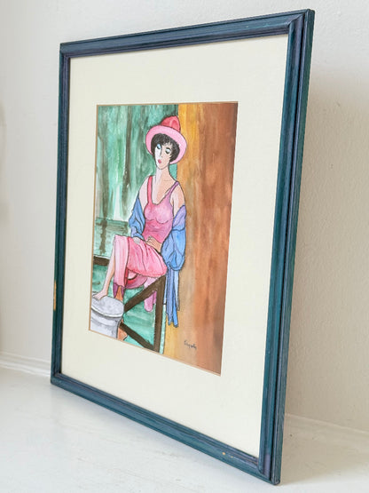Vintage bright watercolour portrait of a seated woman in pink hat and dress with blue jacket, framed in blue wood with off-white mount, photographed on a white surface.