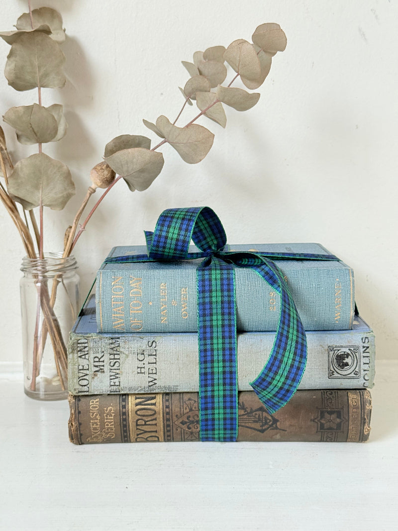 Vintage blue fabric bound decorative book bundle tied with blue and green tartan ribbon, photographed on a white surface