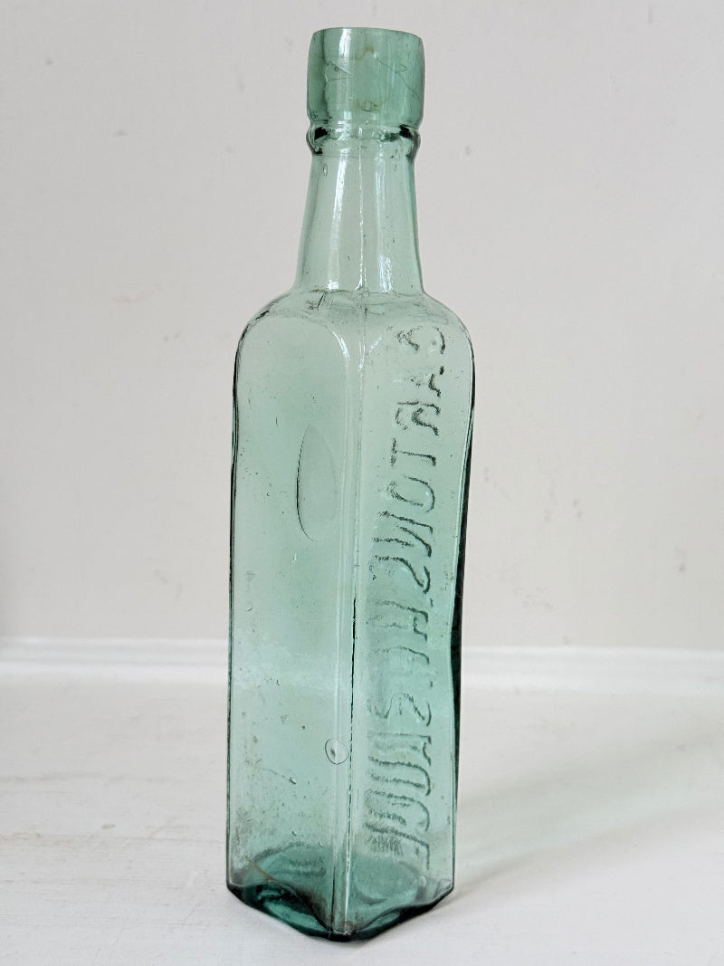 Trio of antique aqua and green glass bottles with embossed lettering, photographed on a white surface