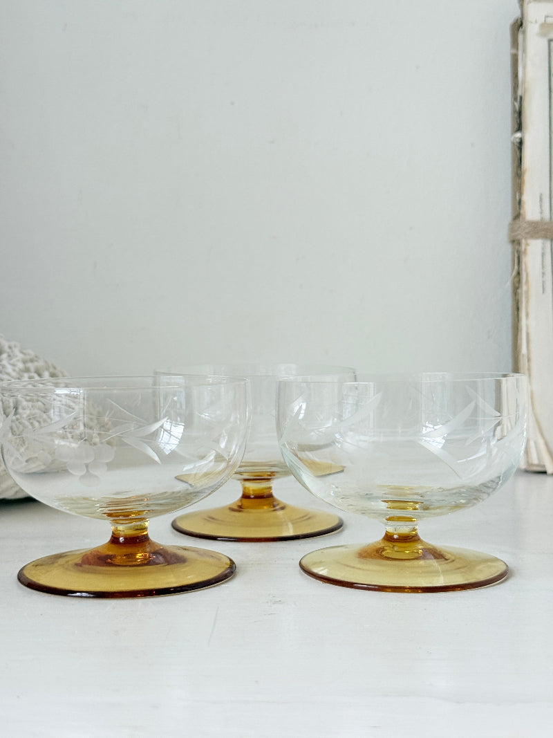 Three clear glass punch bowls with amber-colored bases, arranged on a white surface against a light gray wall.