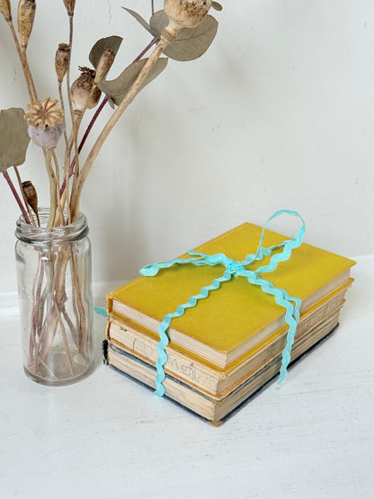 Vintage small decorative book bundle in yellow, brown and grey with turquoise ribbon, photographed on a white surface
