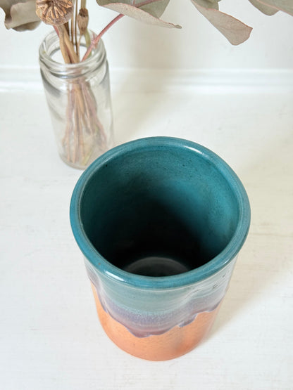 Studio pottery pen pot with teal and plum drip glaze, photographed on a white surface