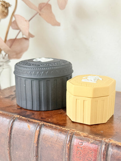 Pair of vintage Wedgwood Jasperware trinket pots in black and yellow with white relief decoration, photographed on a white surface