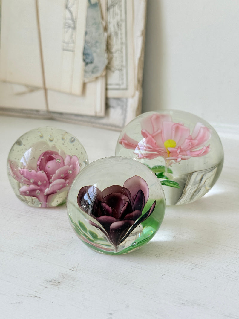 Trio of vintage glass paperweights with hand worked pink and plum floral detail, clear glass domes and green leaf decoration