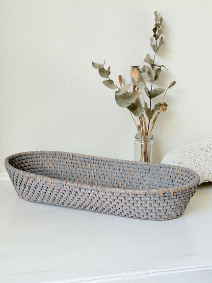 Vintage grey woven bread basket with oval shape and raised rim, photographed on white surface.