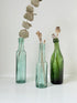 Trio of antique aqua and green glass bottles with embossed lettering, photographed on a white surface