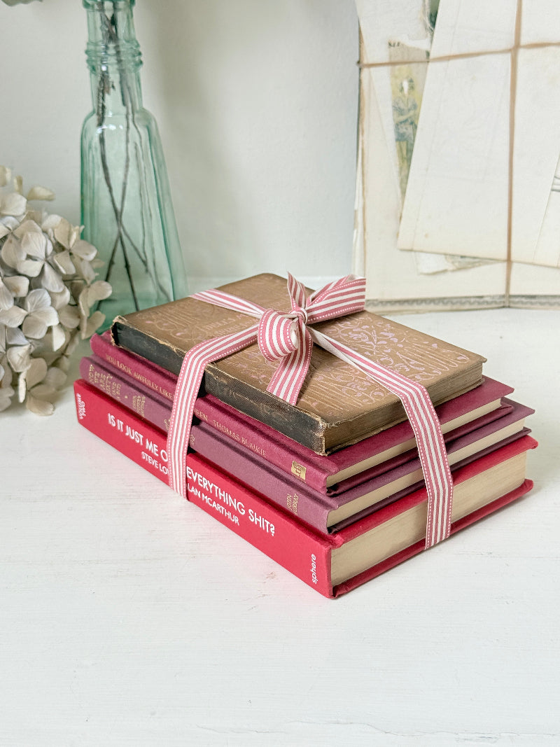 Stack of cloth bound vintage books in red and warm pink tones tied with striped ribbon and dried flowers
