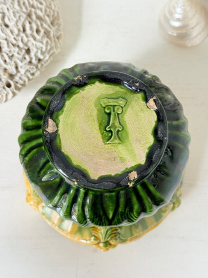 A vintage green glazed ceramic bowl or planter shown from a top-down angle, featuring a dark green outer rim, a lighter green interior, and a central raised monogram letter &