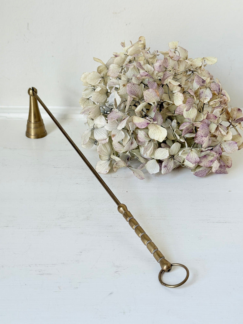 vintage brass candle snuffer with twisted handle and cone-shaped head photographed on white surface