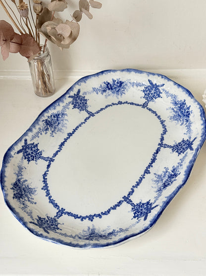 Antique oval blue and white platter with floral border photographed on a white surface