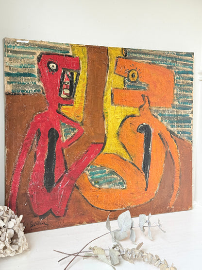 An abstract cubist-style painting on canvas featuring two stylized human figures in red and orange, with yellow and teal background elements, displayed against a white wall with dried flowers in the foreground.