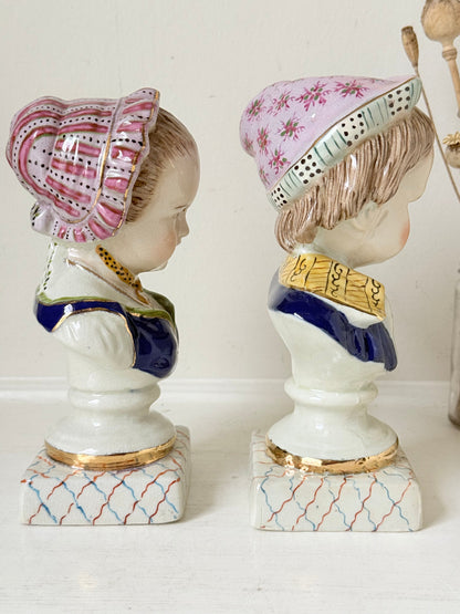 Hand painted Victorian Staffordshire ceramic children busts on white surface, photographed beside dried stems.
