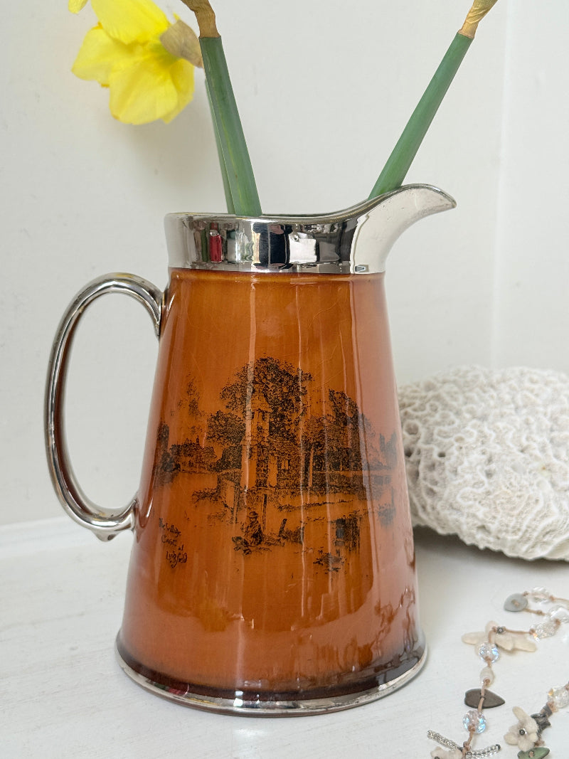 Antique Ridgways stoneware jug photographed on a white surface in amber treacle glaze with black Coaching Days and Coaching Ways scenes and silver lustre rim