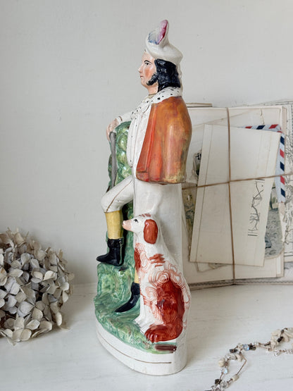 A vintage hand-painted ceramic figurine of a gentleman in profile with a dog, displayed on a white surface with decorative paper and dried flowers in the background.