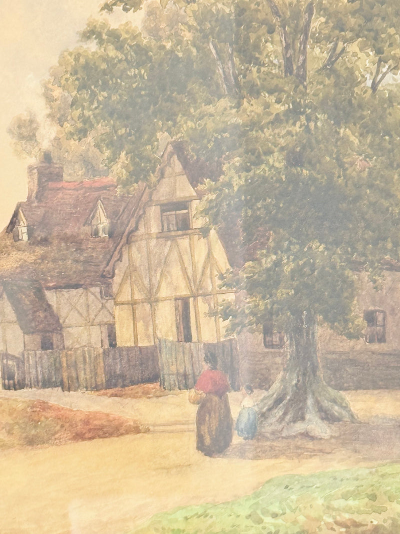 Antique framed watercolour of English village street with thatched cottages and figures, in gilt frame with wide mount, on white surface.