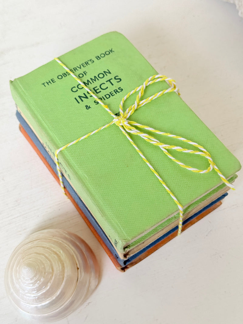 A stack of vintage hardcover books tied with yellow-and-white string, with the top book reading &