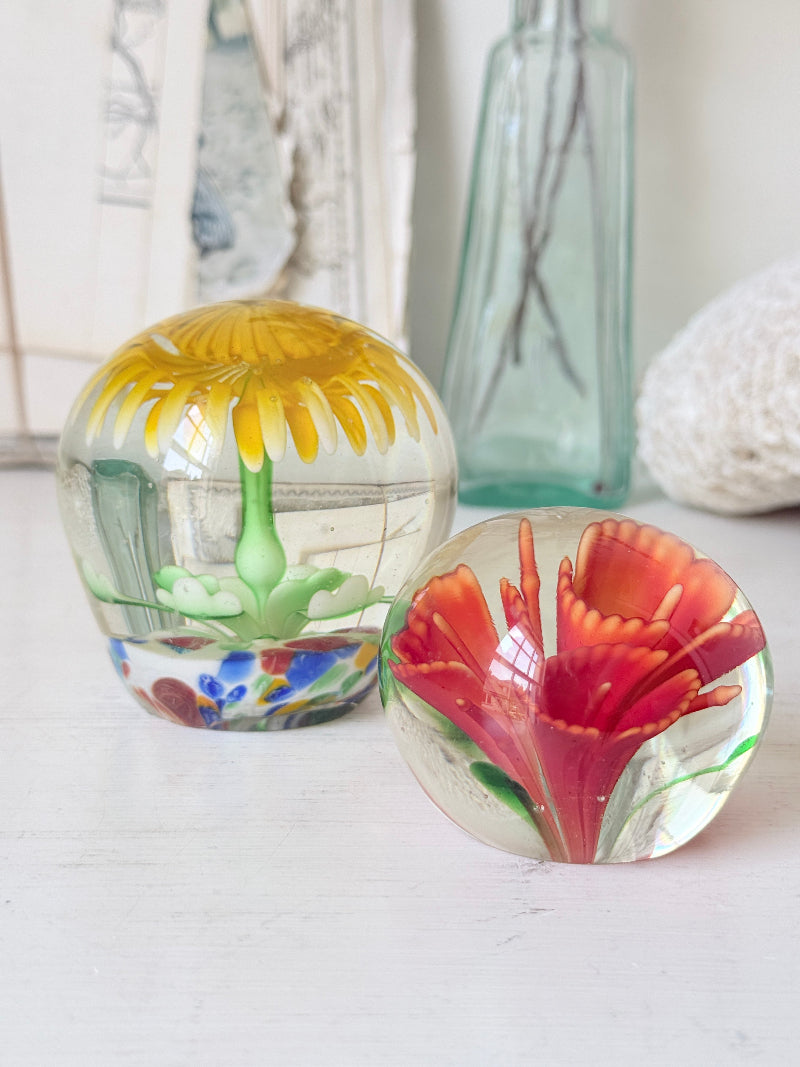 Pair of yellow and red flower glass paperweights with green stems, photographed on a white surface
