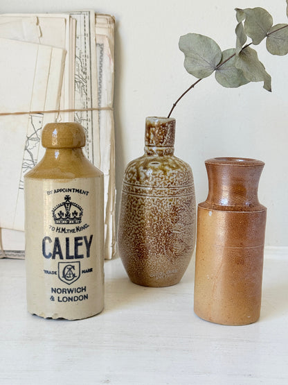 Three antique stoneware bottles, a printed Caley of Norwich and a Portuguese Campos Filhos, photographed on a white surface