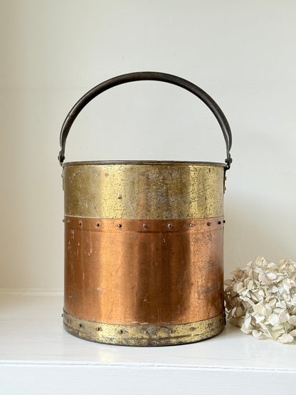 Vintage copper and brass metal bin with handle, photographed on a white surface.