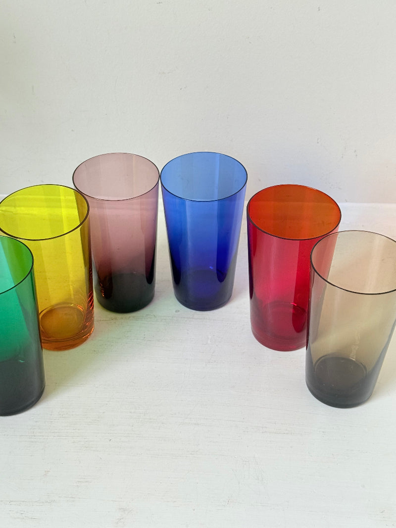 Set of six mid-20th century Boussu coloured glass tumblers in green, yellow, red, violet, blue and brown, photographed on white surface.
