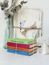 A stack of four hardcover books tied with a string and bow, placed in front of a bundle of vintage papers in a glass bottle vase. The books have colorful spines labeled with titles including &