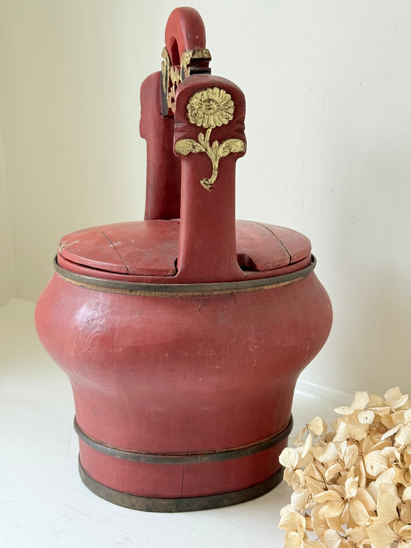 Vintage red painted wooden basket with upright handle and gold painted detail photographed on a white surface