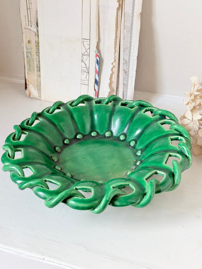 A green ceramic bowl with a decorative, wavy, leaf-like rim and cutout details, displayed on a white surface with vintage books in the background.