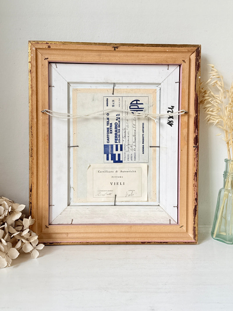 A rustic wooden picture frame with a distressed finish, holding vintage Italian shipping documents and labels, styled on a white surface with dried flowers and a glass vase.