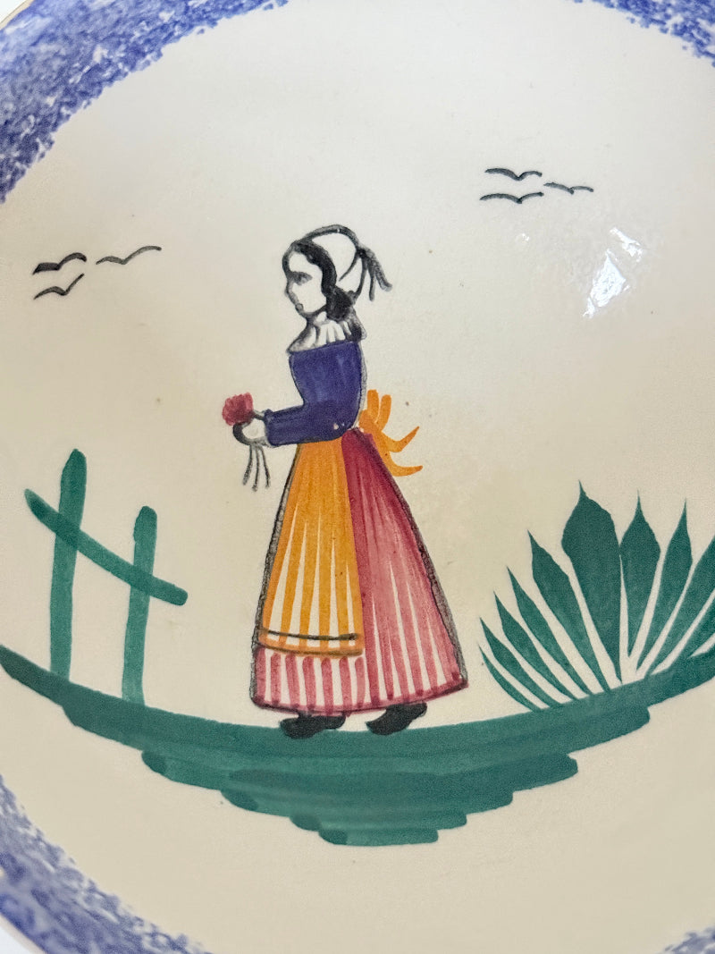 Quimper faience olive bowl with Petit Breton figure and blue speckled rim photographed on a white surface