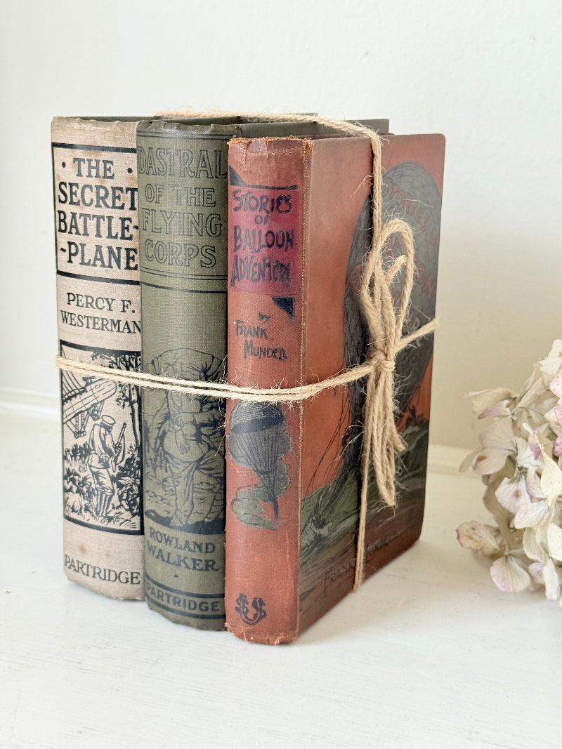Vintage decorative book bundle in red, olive green and cream tied with twine, photographed on a white surface