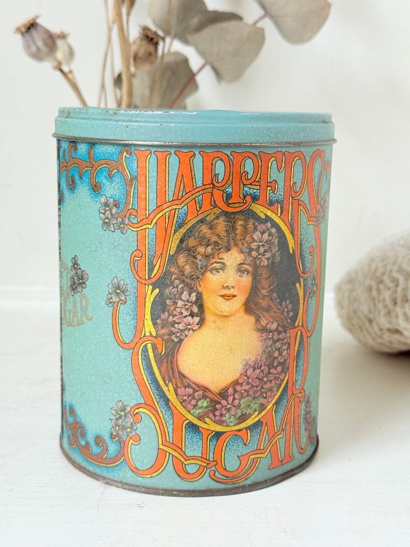 Vintage turquoise and gold metal sweet tin with Art Nouveau woman portrait photographed on a white surface.