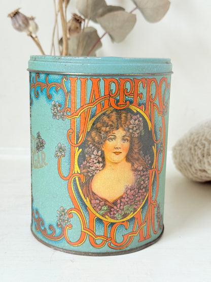 Vintage turquoise and gold metal sweet tin with Art Nouveau woman portrait photographed on a white surface.