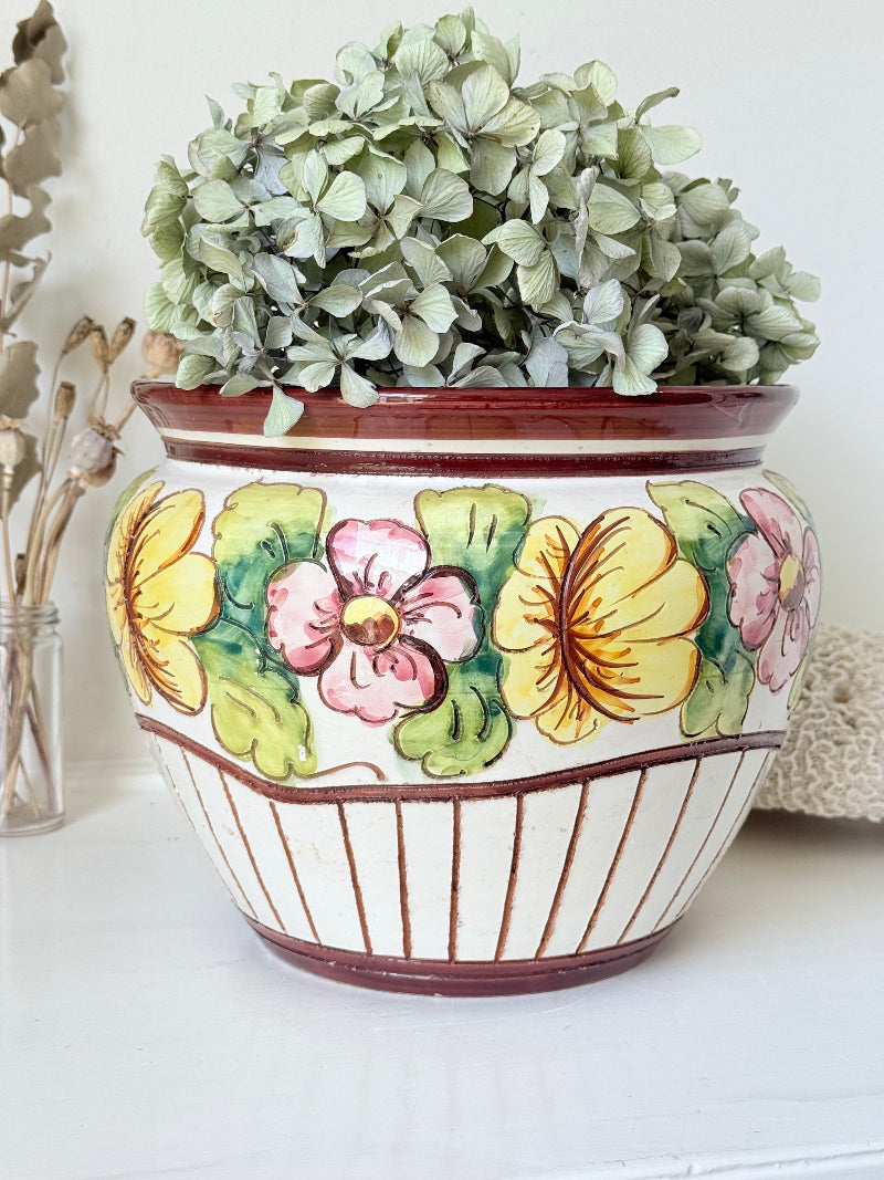 Large European hand painted floral ceramic jardinière with yellow, pink and green flowers on a white base, styled on a white surface with dried foliage.