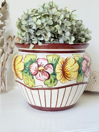 Large European hand painted floral ceramic jardinière with yellow, pink and green flowers on a white base, styled on a white surface with dried foliage.