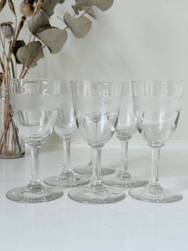 Set of six vintage etched clear glasses with decorative banding, one with a tiny rim chip, photographed on white surface.