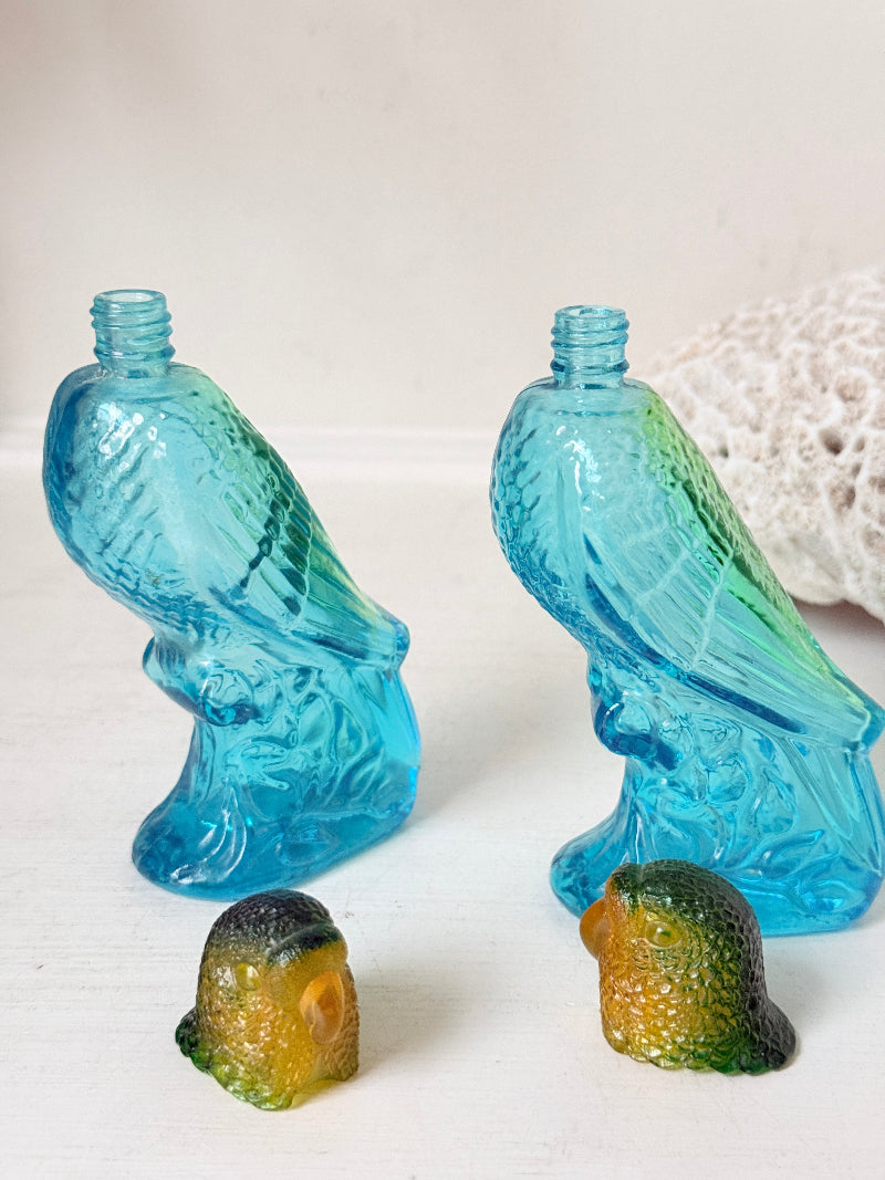 Pair of vintage Avon turquoise glass parrot bottles with green amber stoppers photographed on a white surface