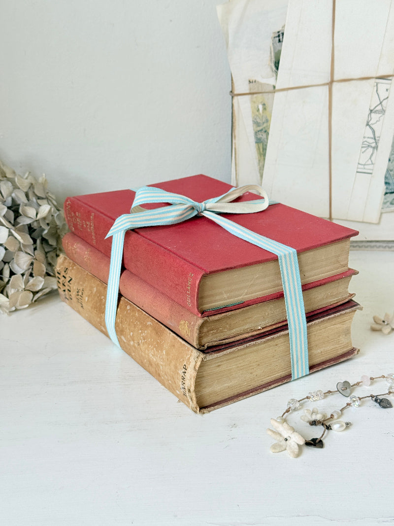 Three antique red books with aged spines tied with a turquoise striped ribbon on a white surface, styled with glass and beads