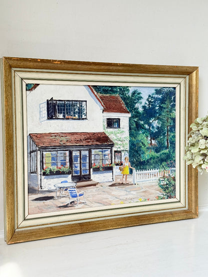 Oil on board painting of a girl in a yellow dress outside a cottage with picket fence, framed, photographed on a white surface