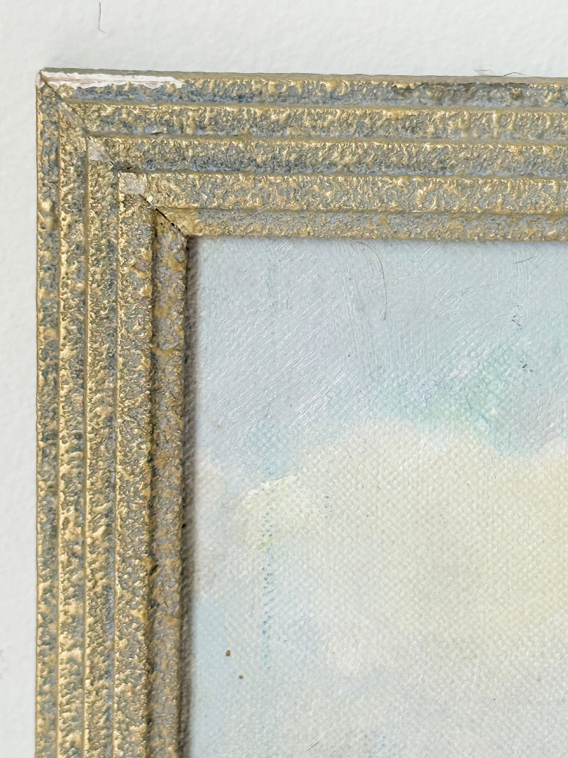 Close-up detail of a textured gold and silver frame with a light blue and white painted canvas visible inside.