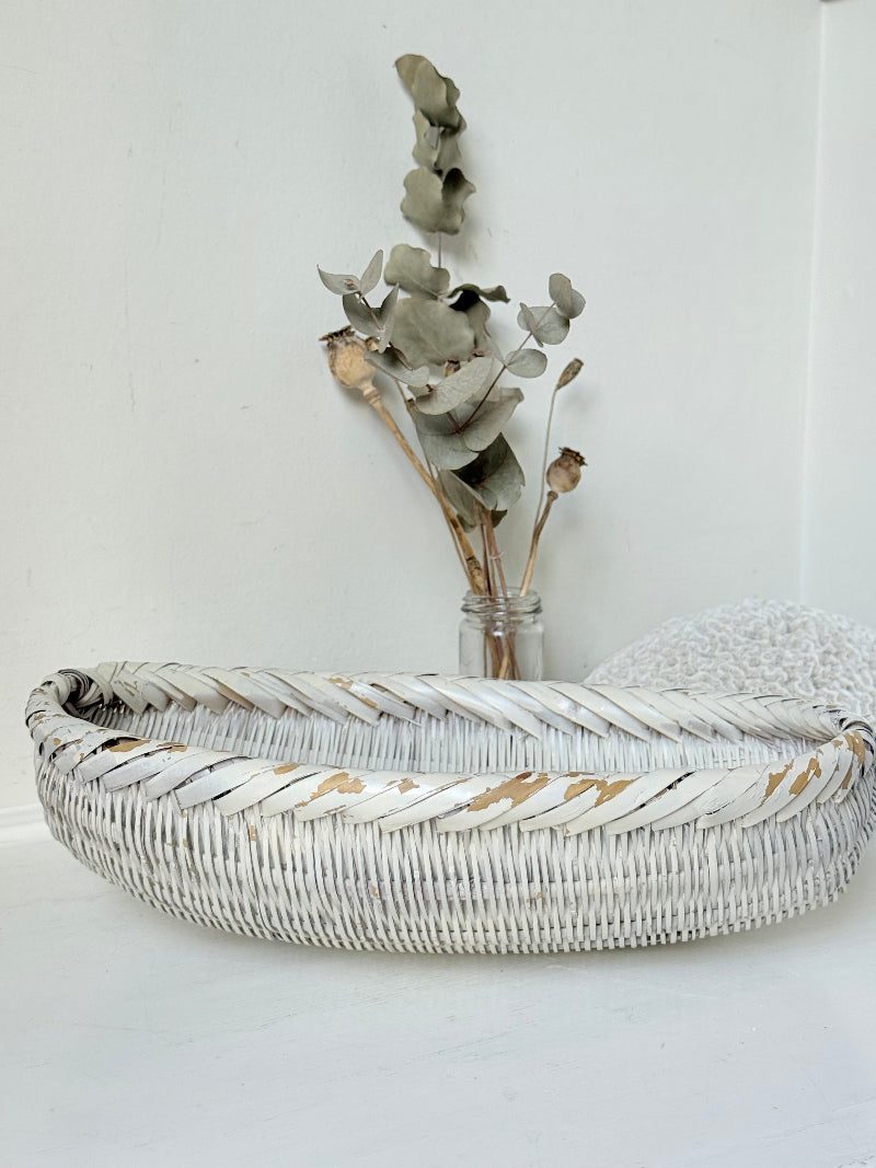 Vintage white chippy wicker basket with oval shape and worn painted finish, photographed on white surface.