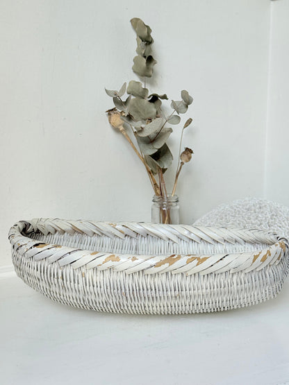 Vintage white chippy wicker basket with oval shape and worn painted finish, photographed on white surface.