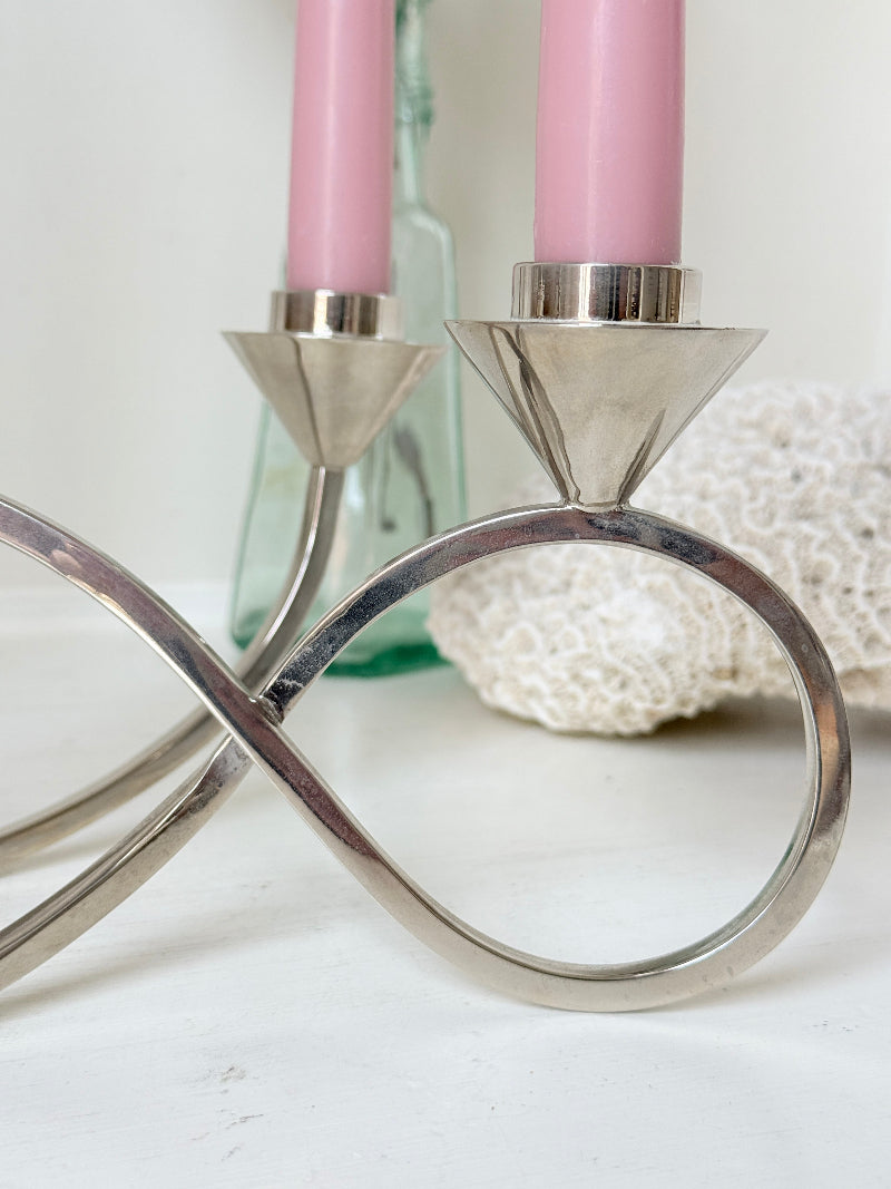 Silver tone five light candelabra with a sculptural looped base holding pink candles, photographed on a white surface