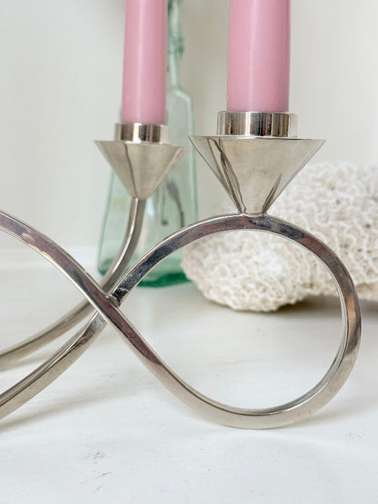 Silver tone five light candelabra with a sculptural looped base holding pink candles, photographed on a white surface
