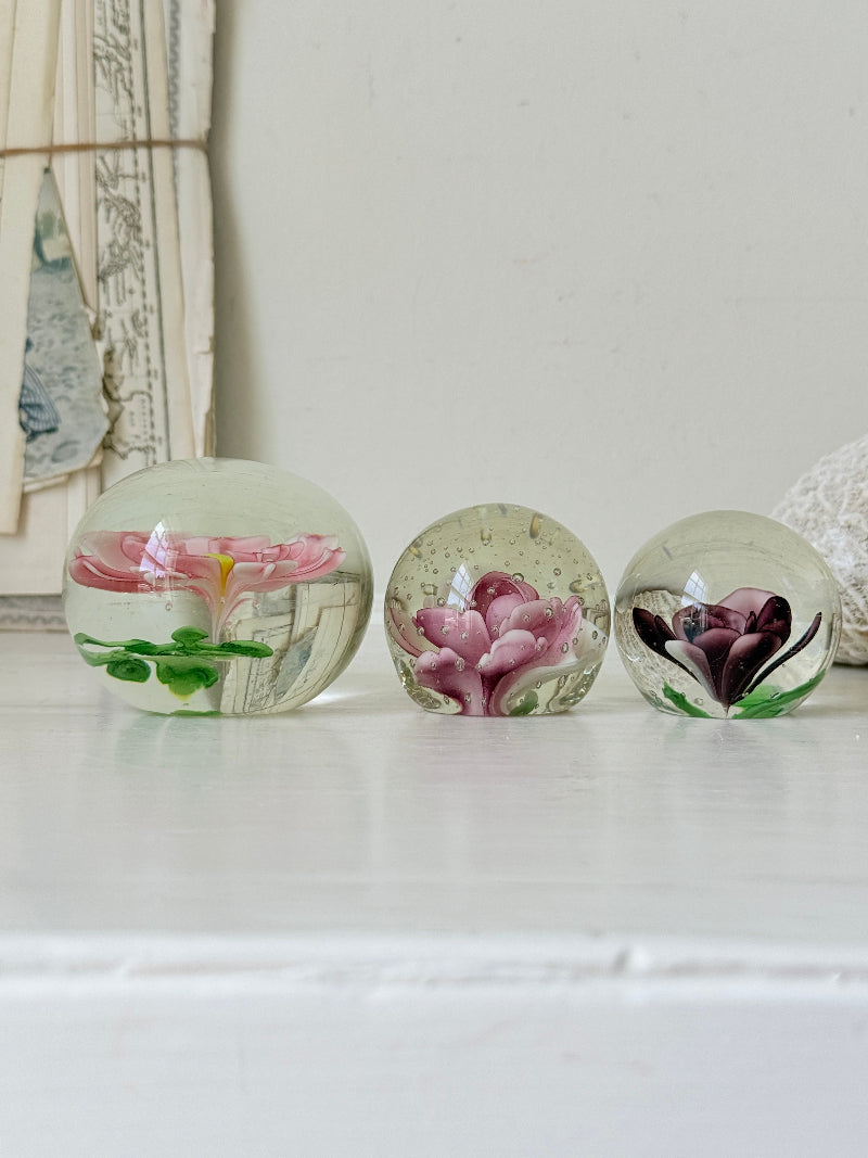 Trio of vintage glass paperweights with hand worked pink and plum floral detail, clear glass domes and green leaf decoration