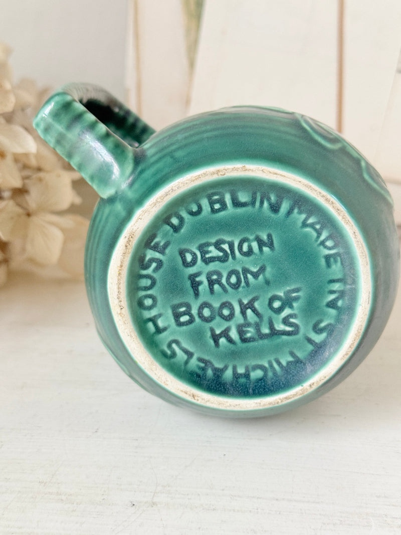 A close-up of the bottom of a teal-green ceramic mug with embossed text reading &