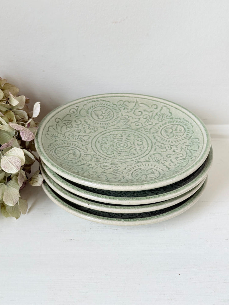Set of four Thai celadon side plates with embossed patterns and sage green crackled glaze, stacked and photographed on white surface