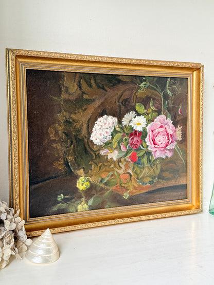 A framed oil painting of a floral still life, featuring pink and white roses with green leaves, housed in an ornate gold frame, displayed on a white surface.