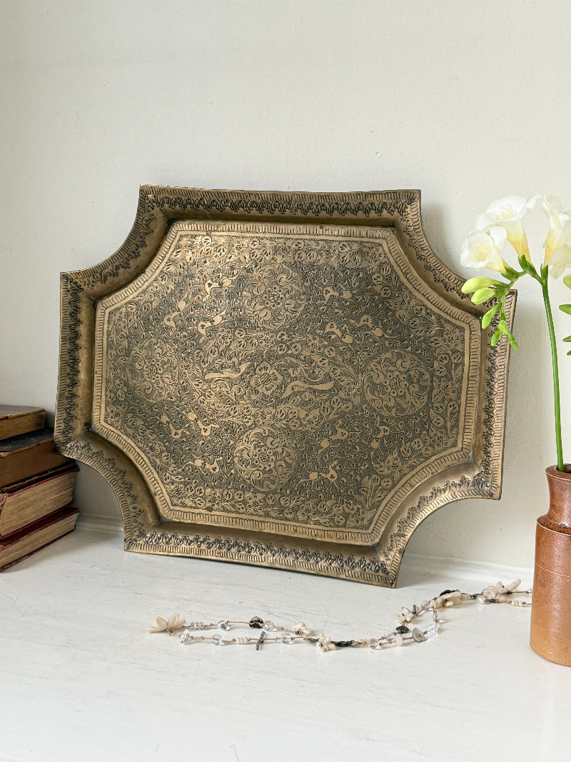 Vintage hand engraved brass wall plaque with floral scrollwork, figural decoration, shaped edge and aged patina