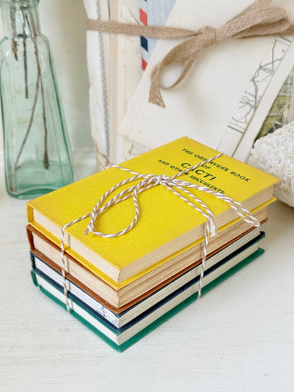 A stack of hardcover books tied with twine, featuring a bright yellow top book titled &