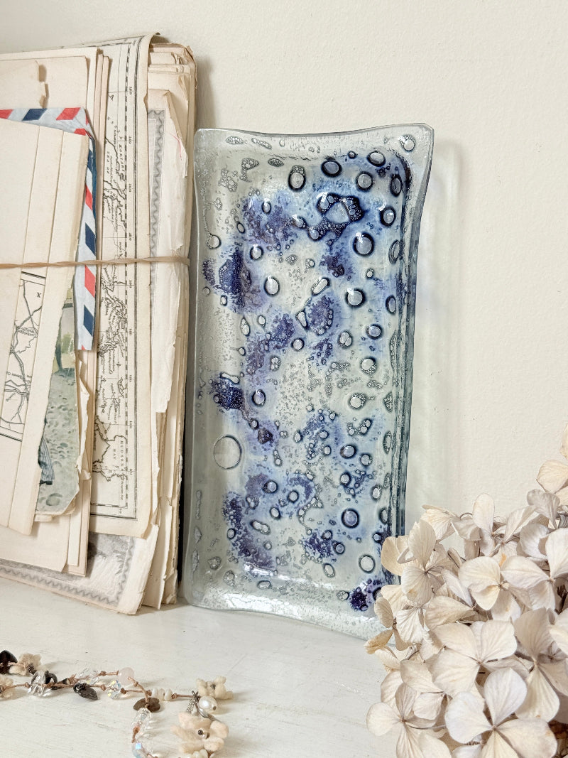 A rectangular glass tray with a blue and white spotted pattern, styled on a tabletop next to vintage letters and dried flowers.